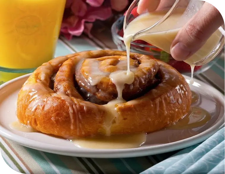 A glazed cinnamon roll with melting butter icing, served beside orange juice and fresh berries