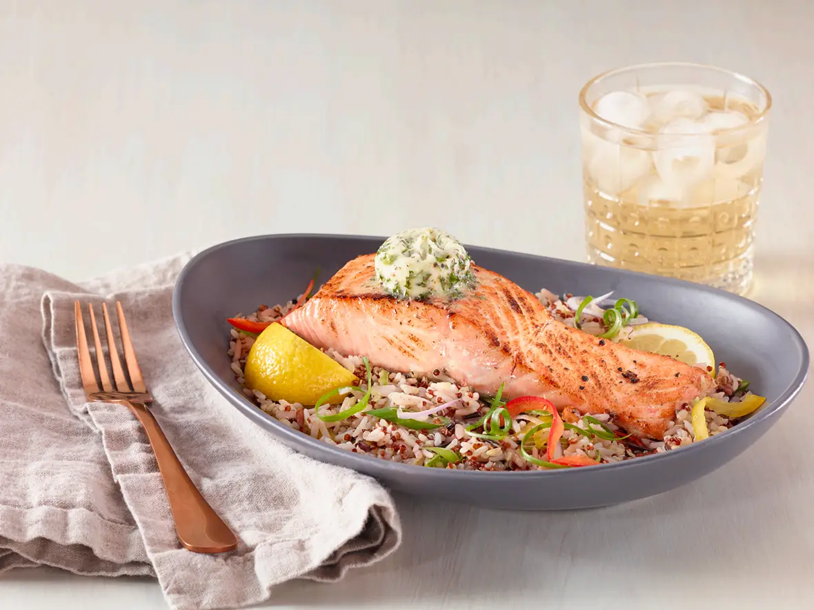 A seared fish fillet finished with herb butter, served over yellow rice with broccolini and carrots
