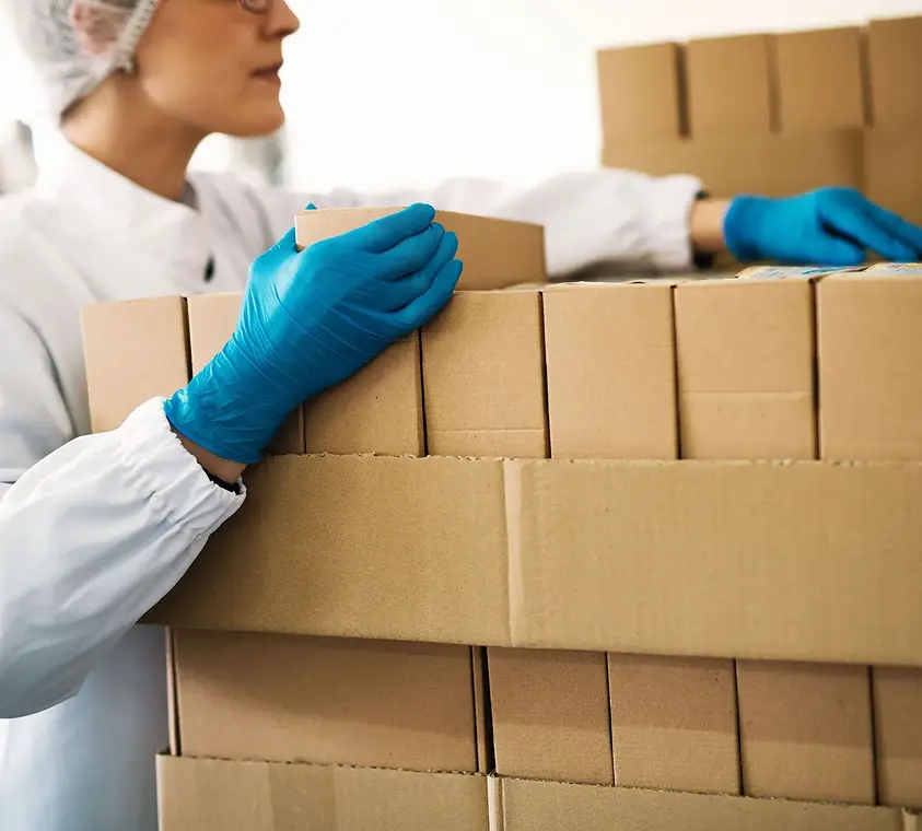 A worker in a lab coat and gloves stacking finished cartons for distribution
