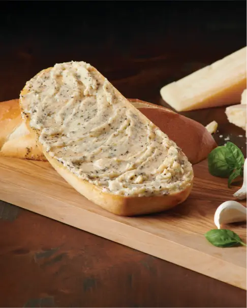 A loaf of bread spread with herb butter on a wooden board with garlic