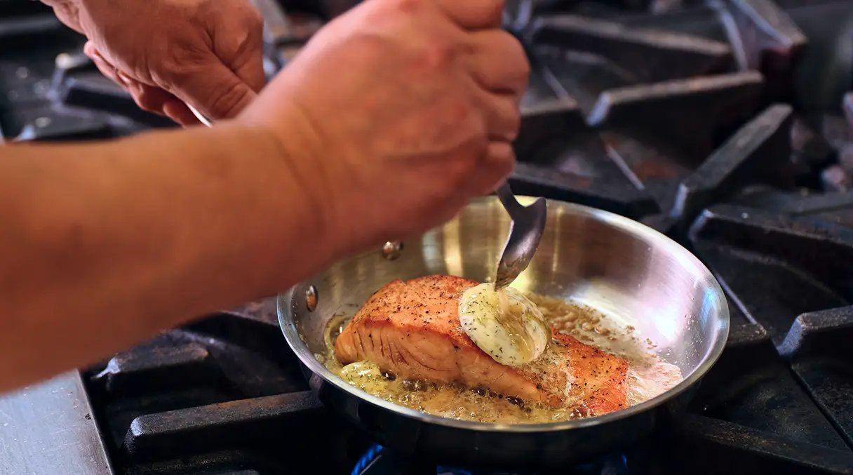 A chef finishing a cream sauce in a sauté pan on a restaurant line
