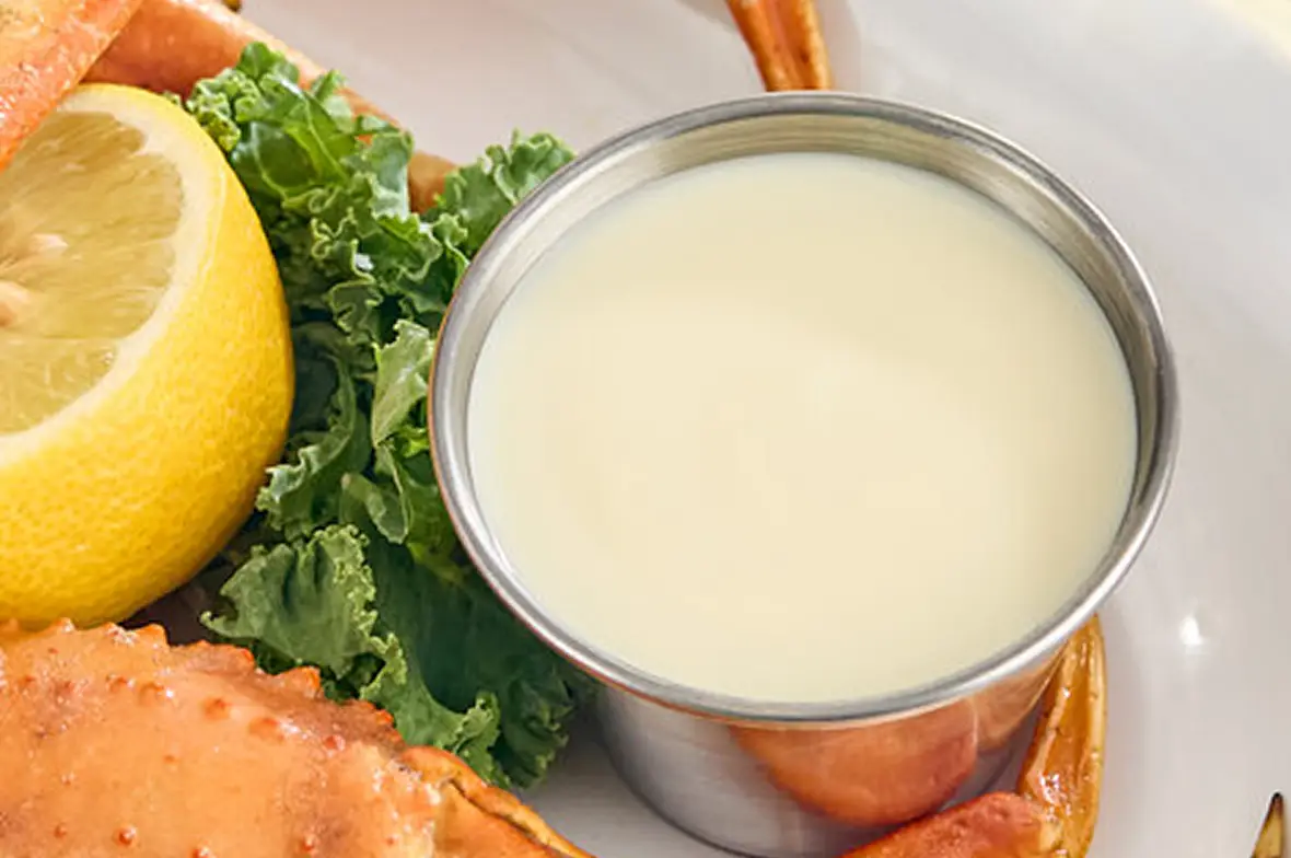 A rich butter sauce being finished in a pan beside fresh lemons and herbs