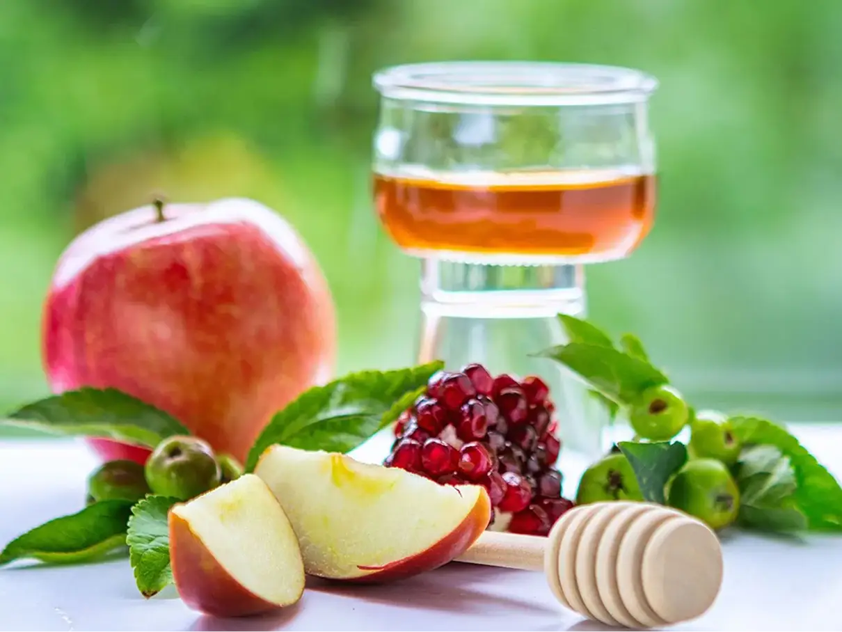 Fresh apple, pomegranate and a glass of amber glaze with a honey dipper