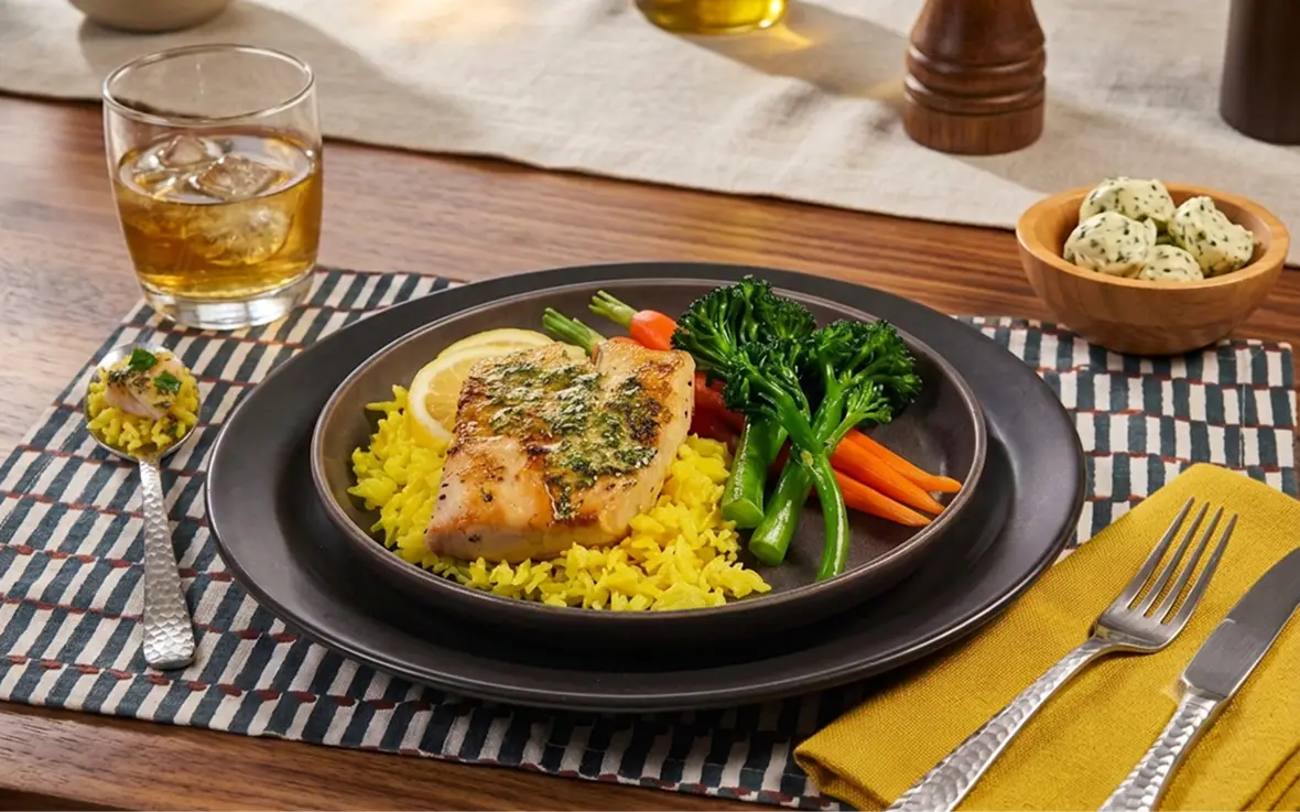 Glazed fish over yellow rice with carrots and broccolini, a bowl of herb margarine dollops alongside