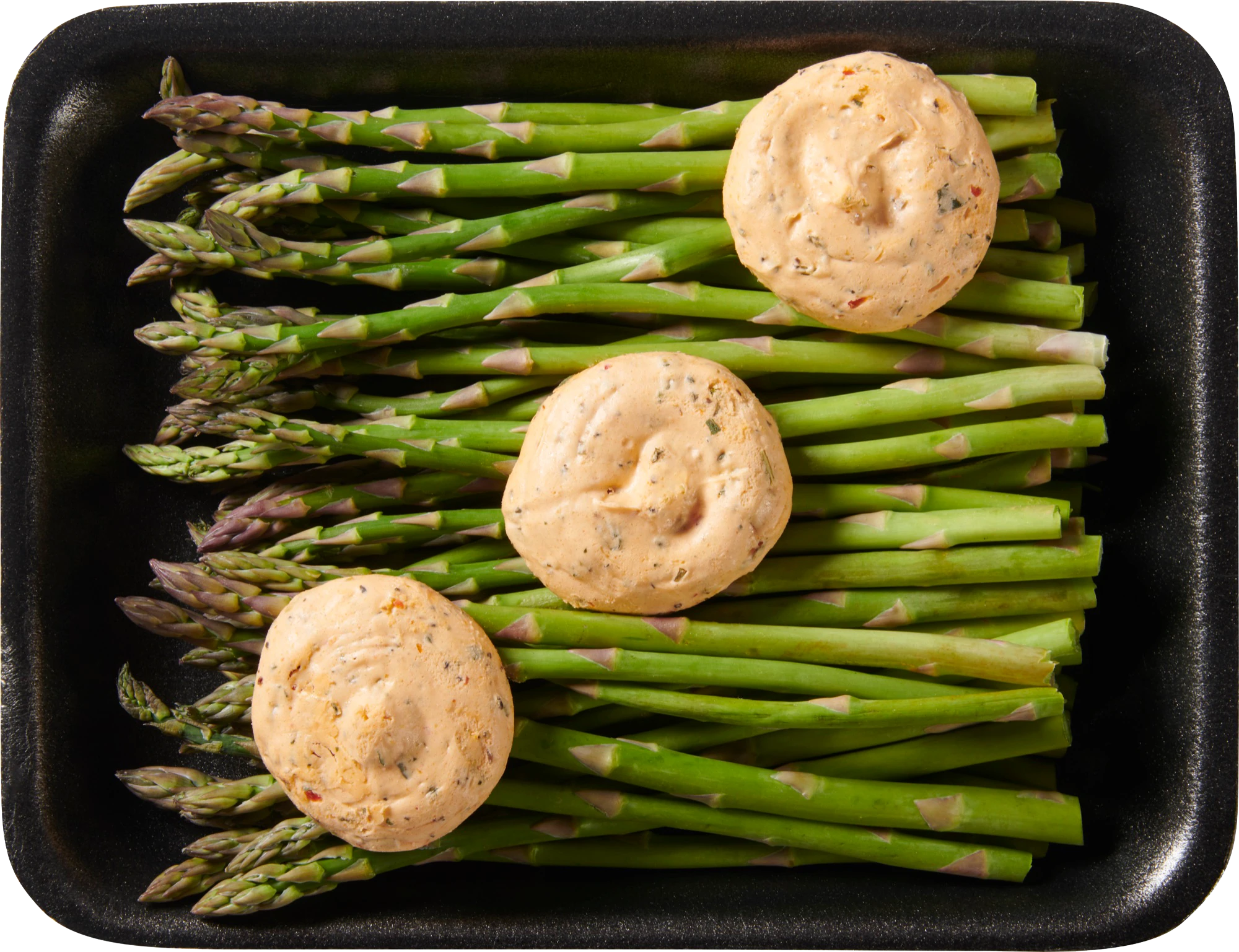 Asparagus spears in a black tray topped with herb butter dollops