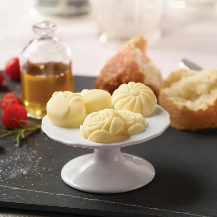 Assorted rose and flower-shaped butters on a pedestal dish with bread and tomatoes