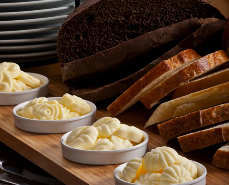 Assorted shaped butters in bowls beside sliced bread on a board