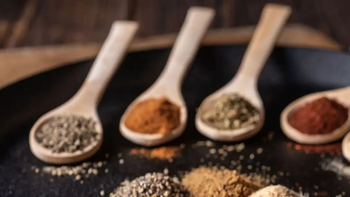 Assorted spices in wooden spoons on a dark surface