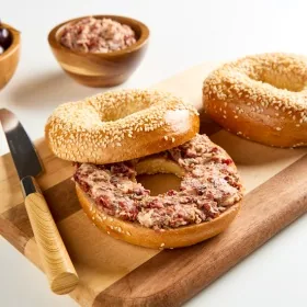 Bagel sandwich with red pepper spread on a wood cutting board