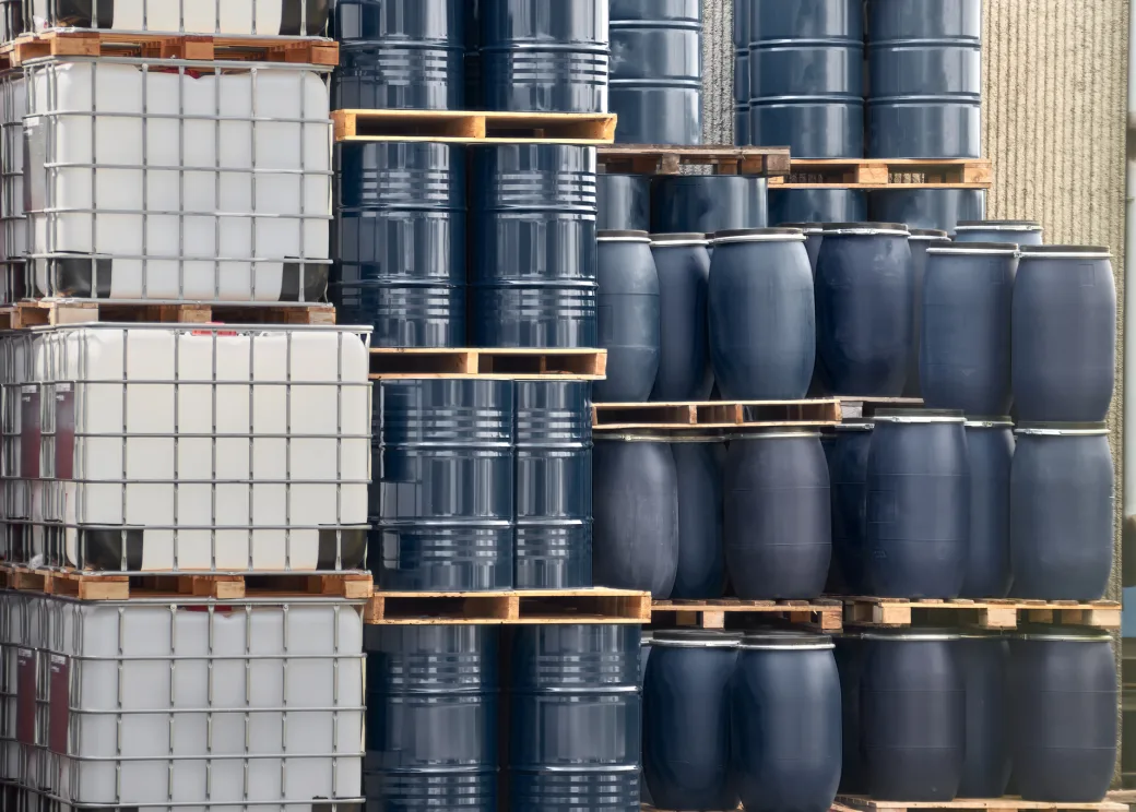 Steel drums, plastic barrels and white totes stacked on pallets