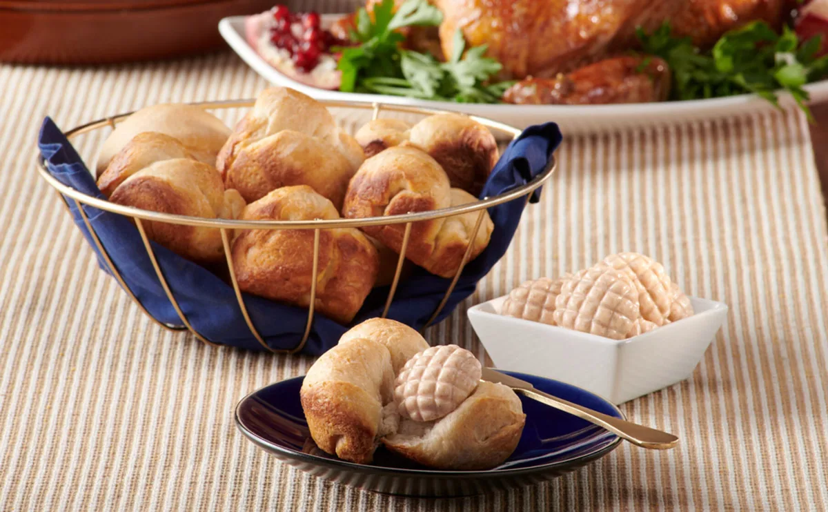 Bread rolls in a basket with honeycomb-shaped butter and roast turkey