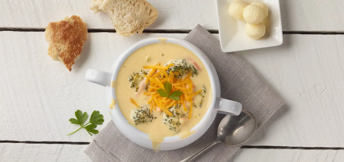 Bowl of broccoli cheddar soup with bread and a dish of butter balls