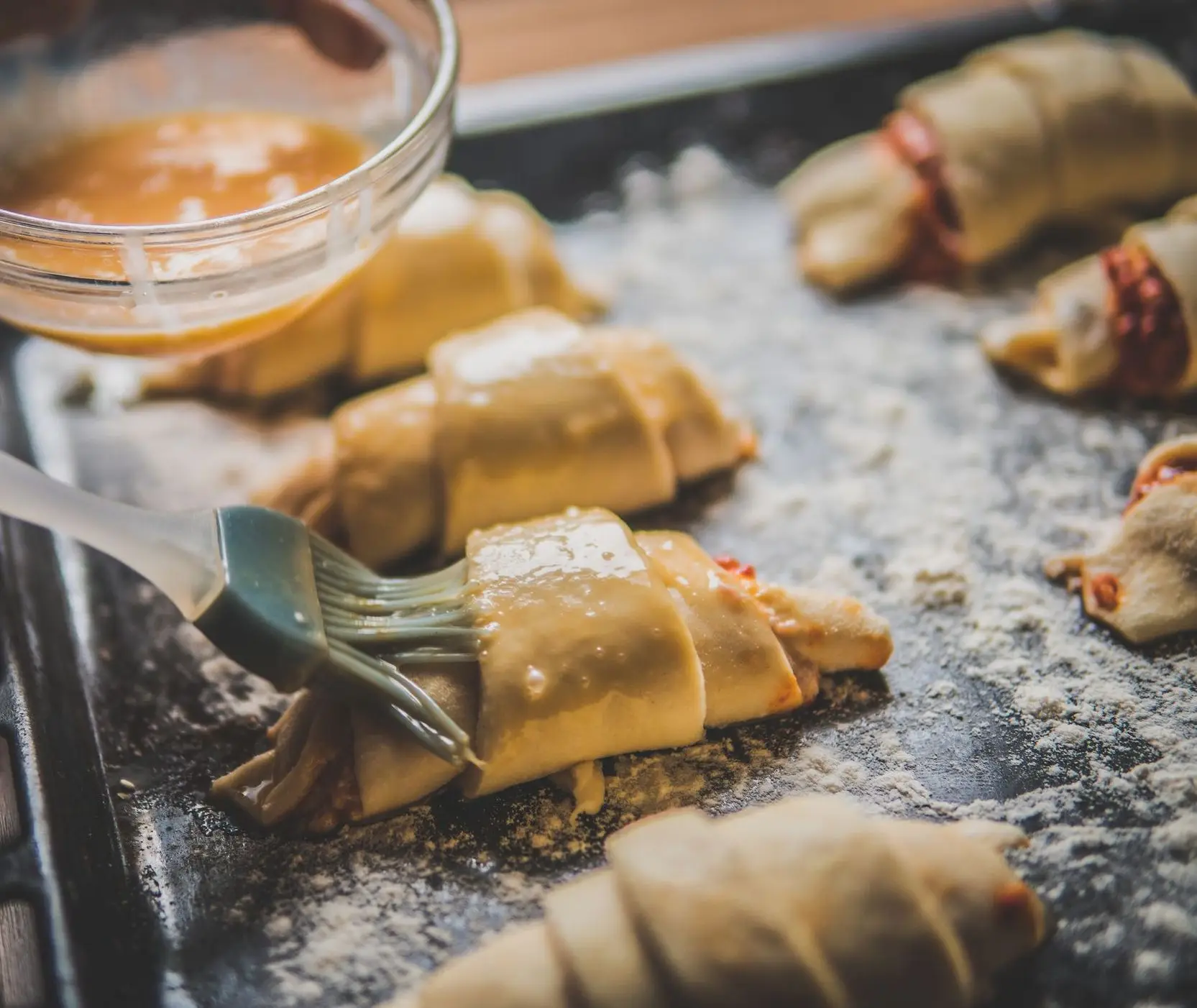 Brushing an amber glaze onto filled crescent rolls on a floured baking sheet
