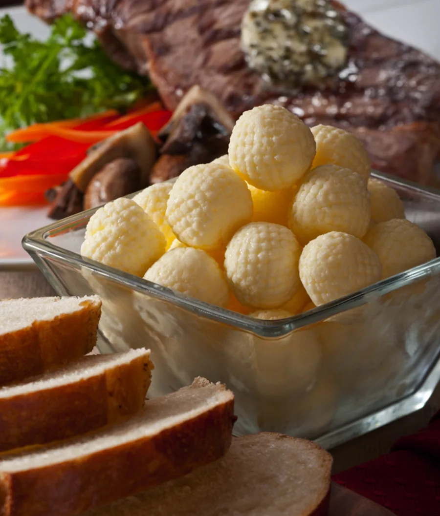 Textured butter balls in a glass dish beside sliced bread and a grilled steak