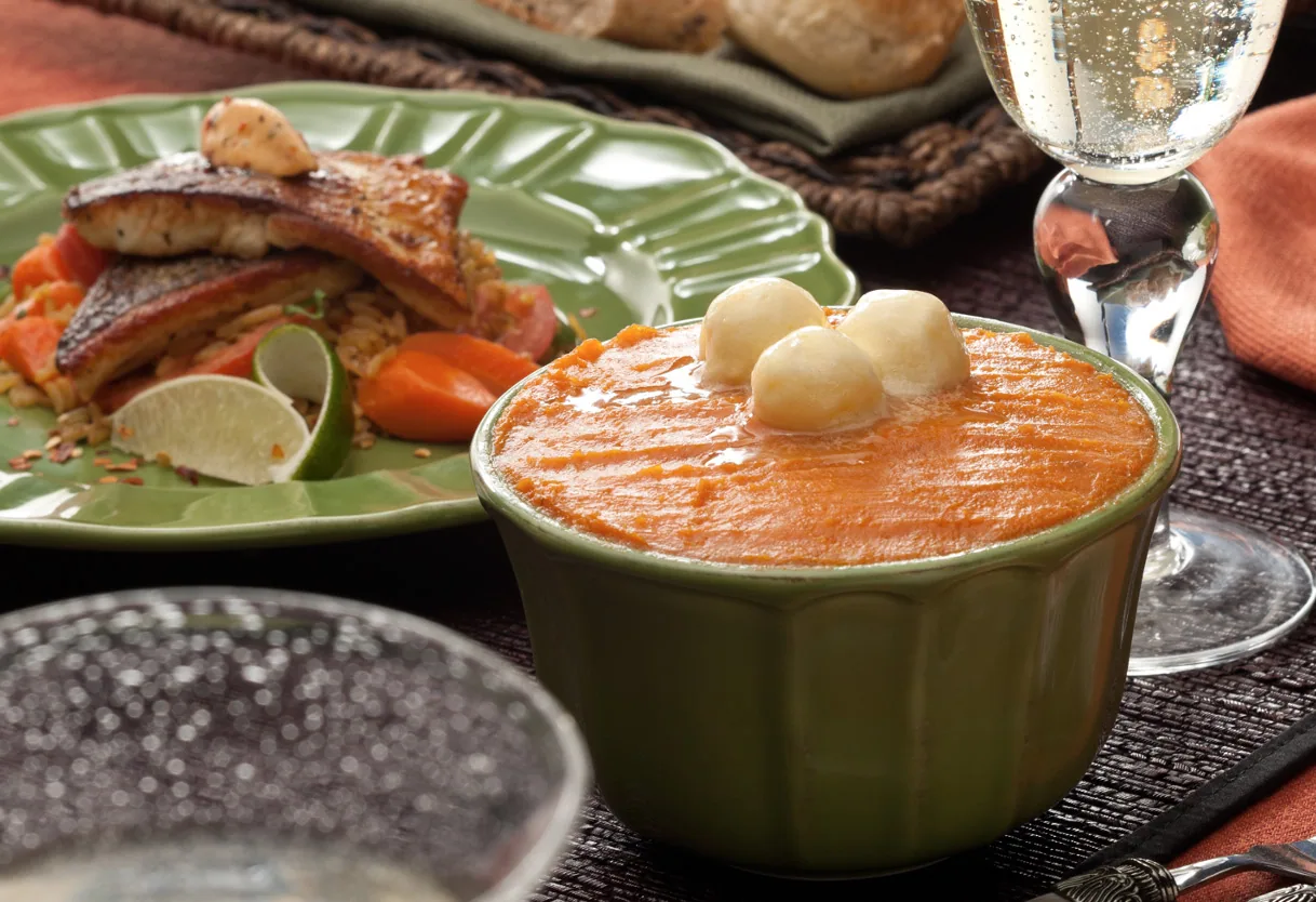 Three pale butter balls atop orange puree beside a plate of blackened fish