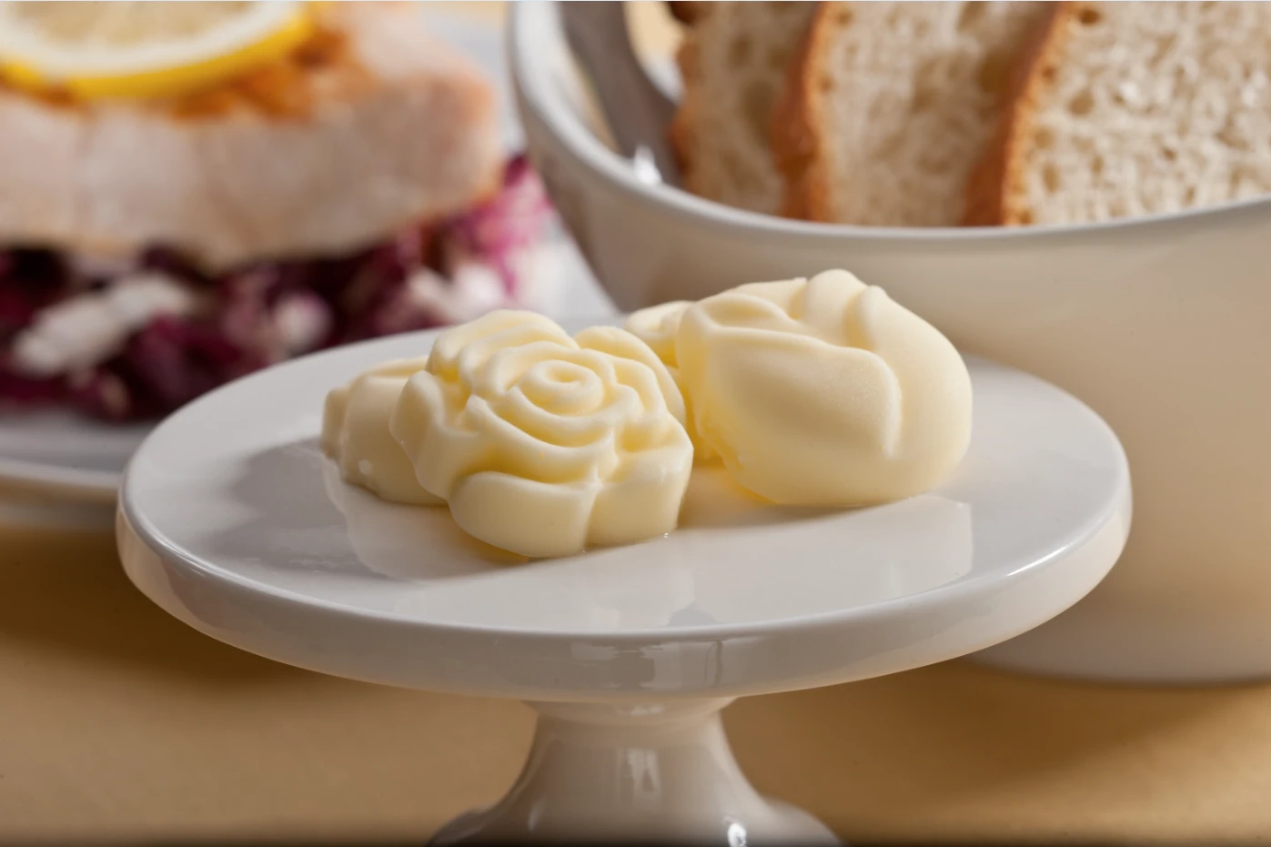 Two butter roses on a pedestal cake stand beside a bread basket