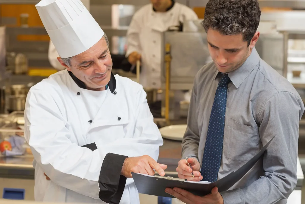 Chef consulting with a manager holding a clipboard in a commercial kitchen