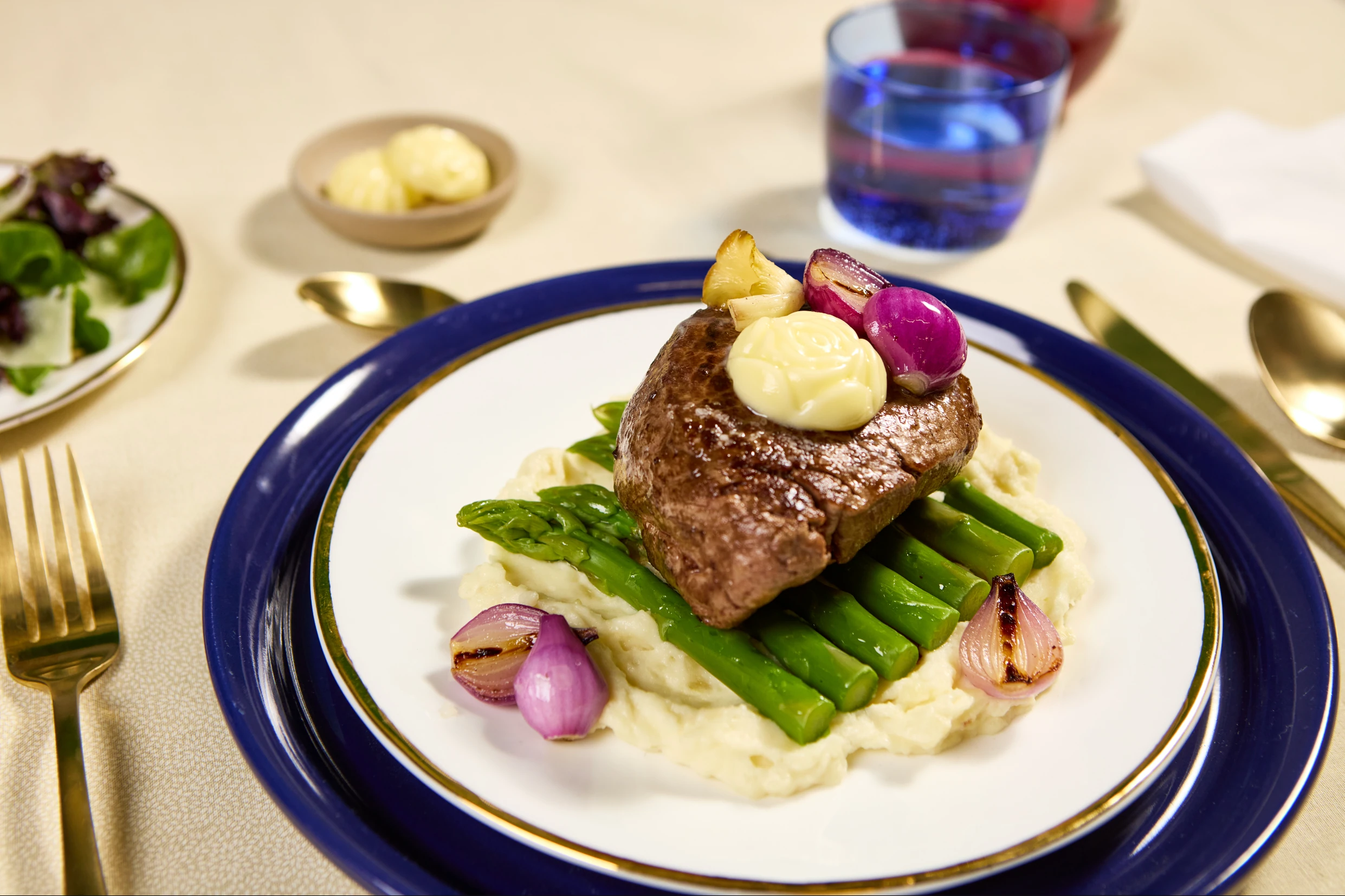 Filet steak topped with rose-shaped butter on mashed potatoes and asparagus