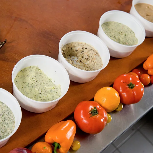 Cups of flavored butter beside fresh tomatoes and peppers