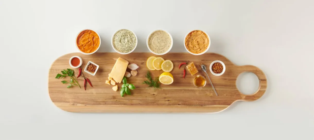 Wooden board with flavored butter dips, cheese, herbs and spices