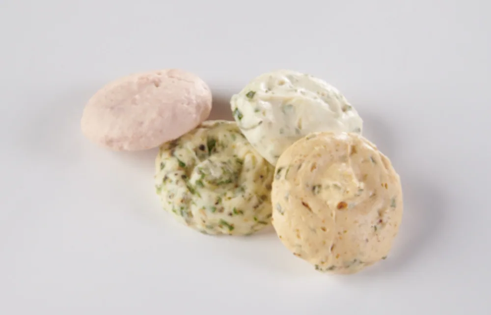 Four flavored butter dollops in different colors on white