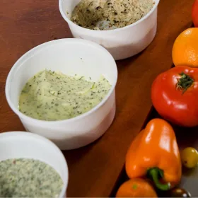 Three bowls of flavored butter sauce beside tomatoes and peppers