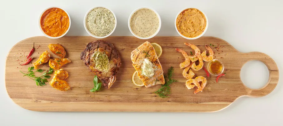 Four bowls of flavored butter sauce with grilled meat, herbs and vegetables