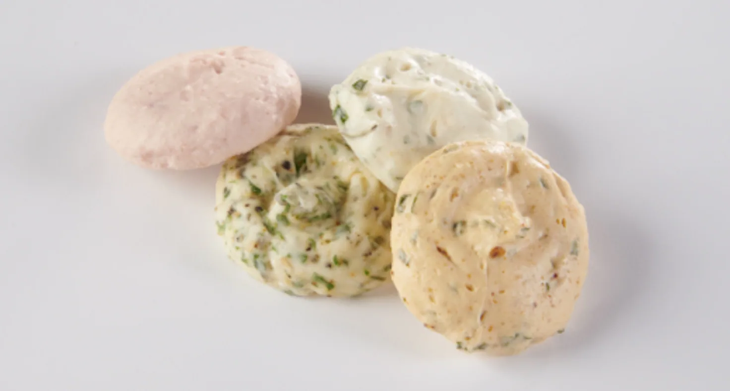 Four flavored butter dollops in pink, herb, cream and tan on a white background