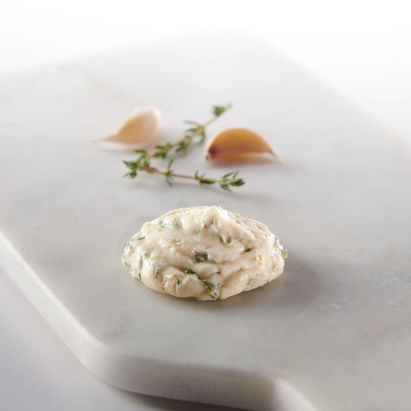 Garlic herb butter dollop on a marble board with garlic cloves and thyme