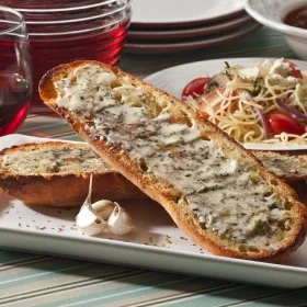 Garlic herb toast slices on a plate with a whole garlic clove
