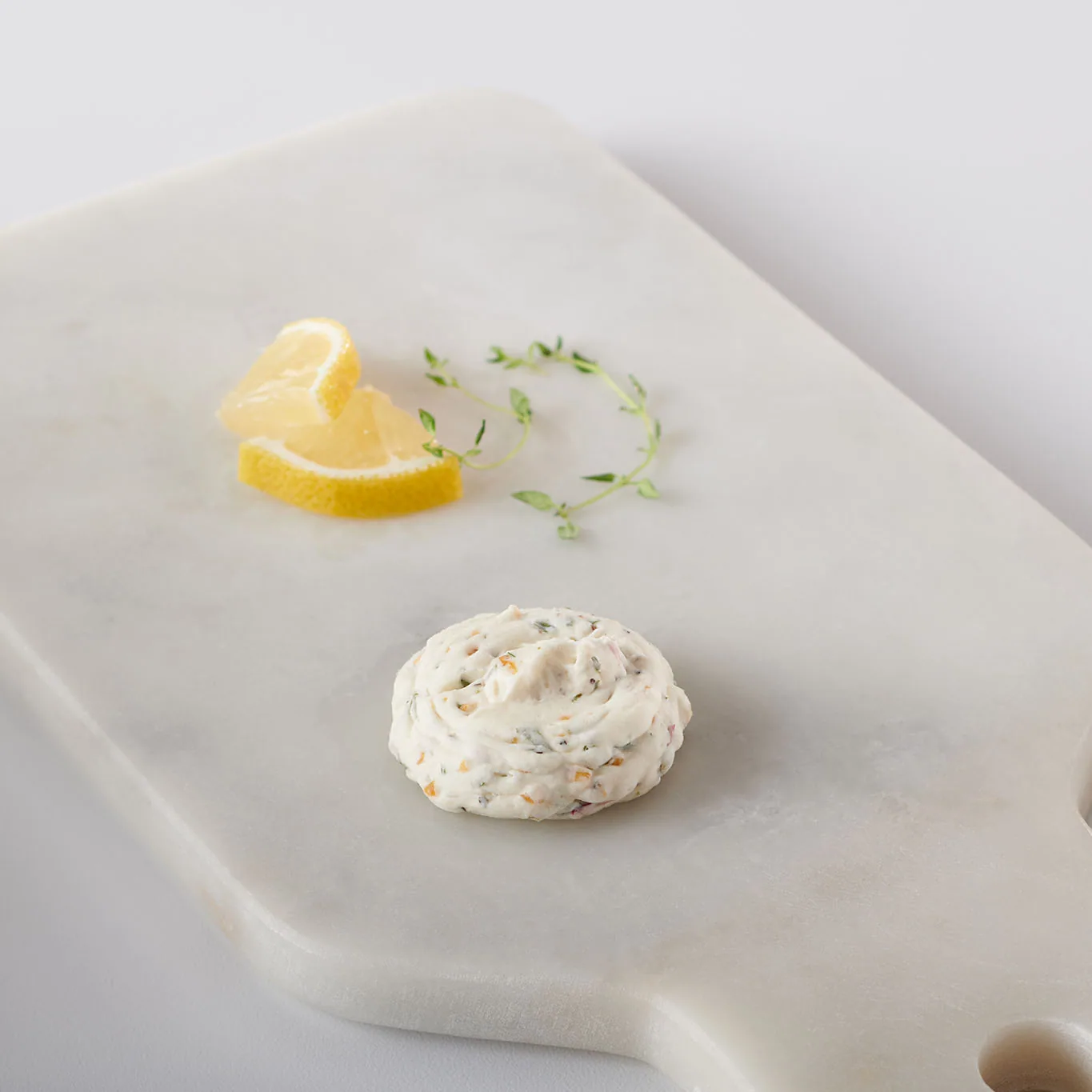 Single herb butter dollop with lemon wedges and thyme on a marble board
