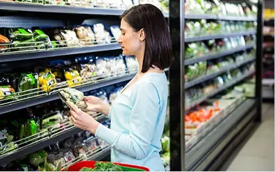 A shopper selecting fresh packaged produce in a refrigerated retail aisle