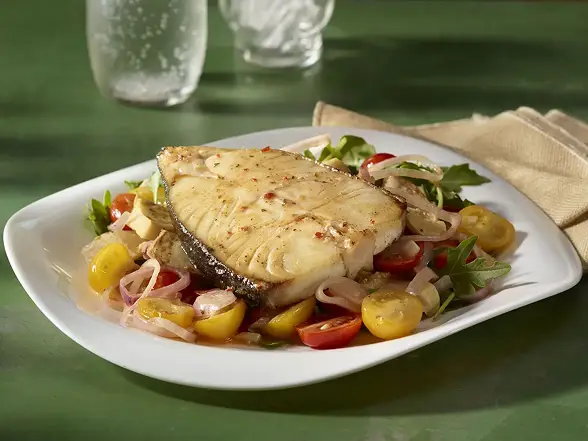Grilled marinated fish steak over an arugula, cherry tomato, and shallot salad on a white plate