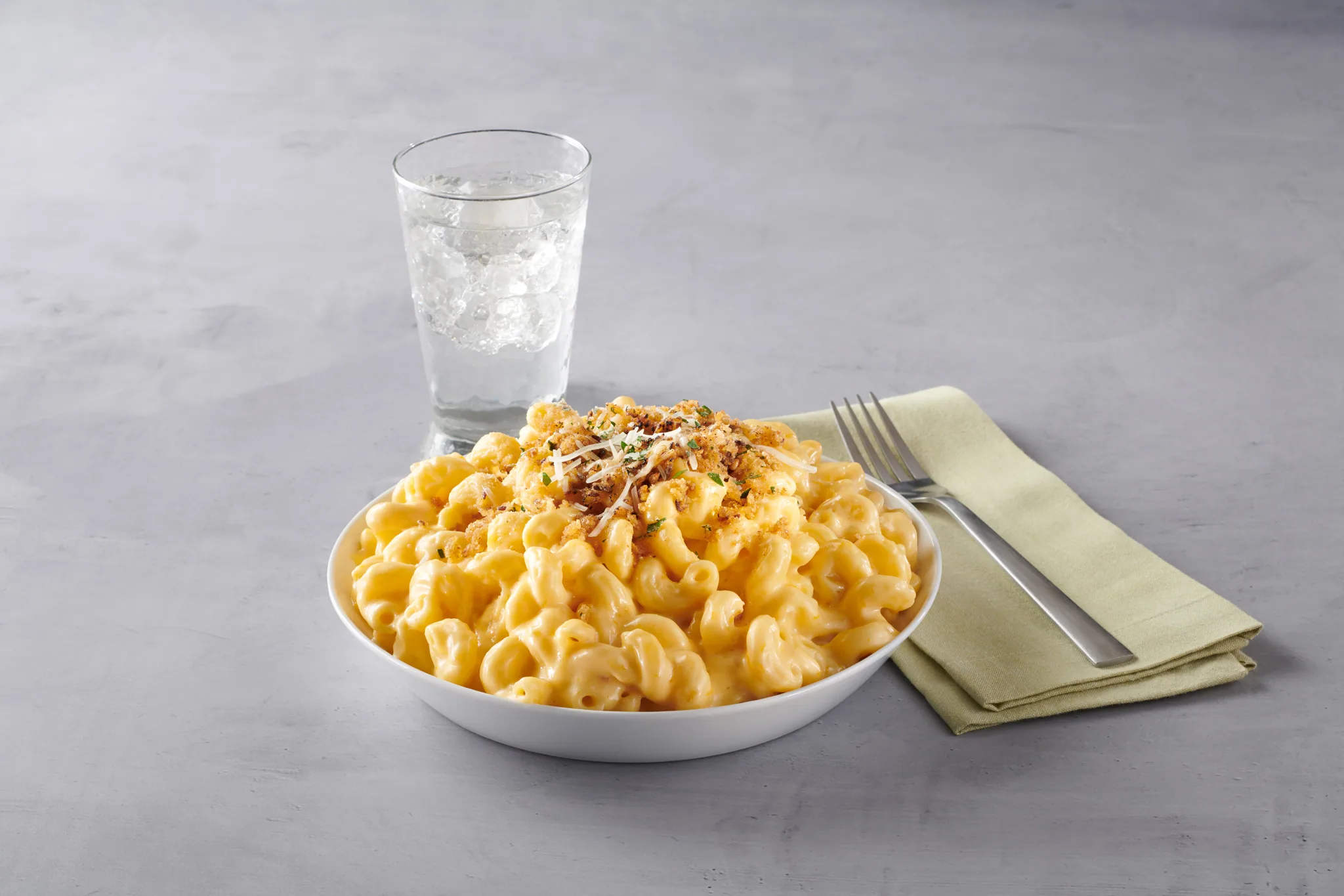 Bowl of macaroni and cheese topped with breadcrumbs, with a glass of water