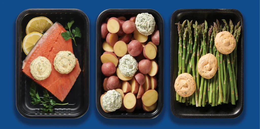 Meal kit trays of salmon, potatoes and asparagus with butter on blue