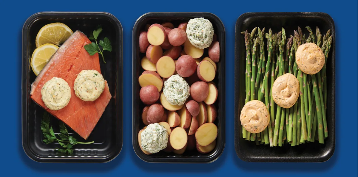Meal kit trays of salmon, potatoes and asparagus with butter on blue