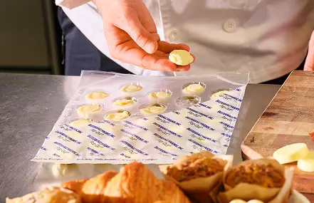 Hand placing a butter portion into individual wrap packaging beside croissants