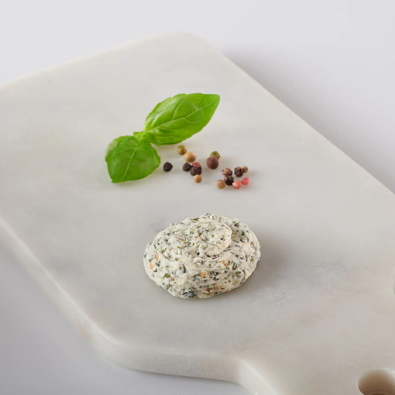 Pesto basil butter dollop on a marble board with basil leaf and peppercorns