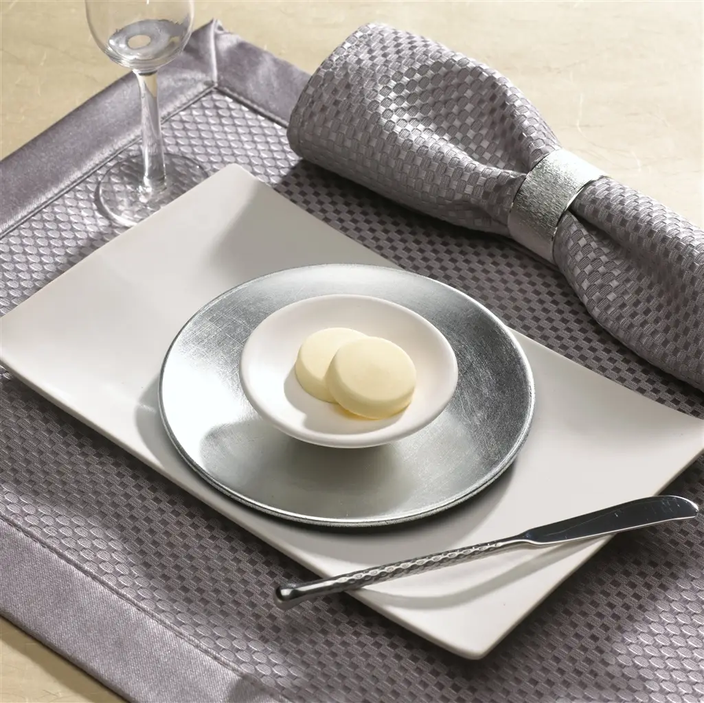 Two Pop-Out butter medallions in a white dish on a silver charger beside a wine glass and napkin