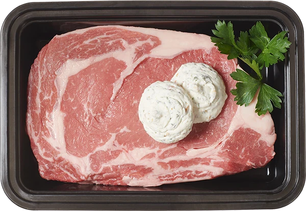 Raw steak in a tray topped with two herb butter dollops and parsley