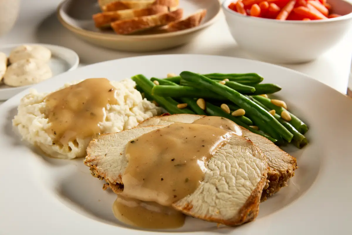 Sliced roast turkey and mashed potatoes topped with gravy beside green beans and pine nuts