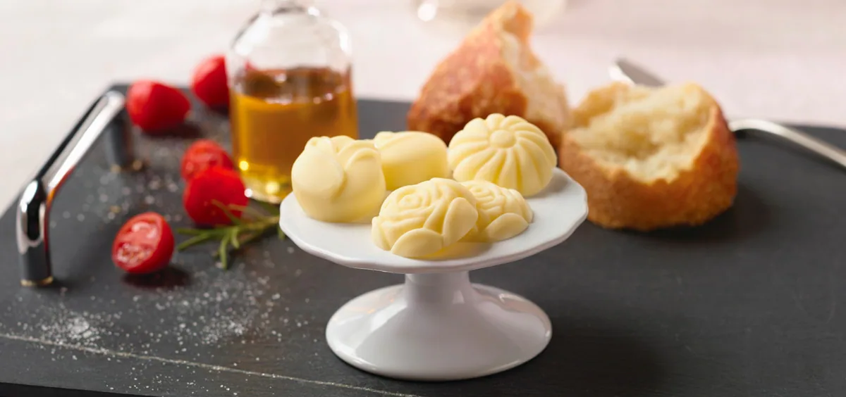 Rose-shaped butter pieces on a pedestal plate with bread, tomatoes and oil