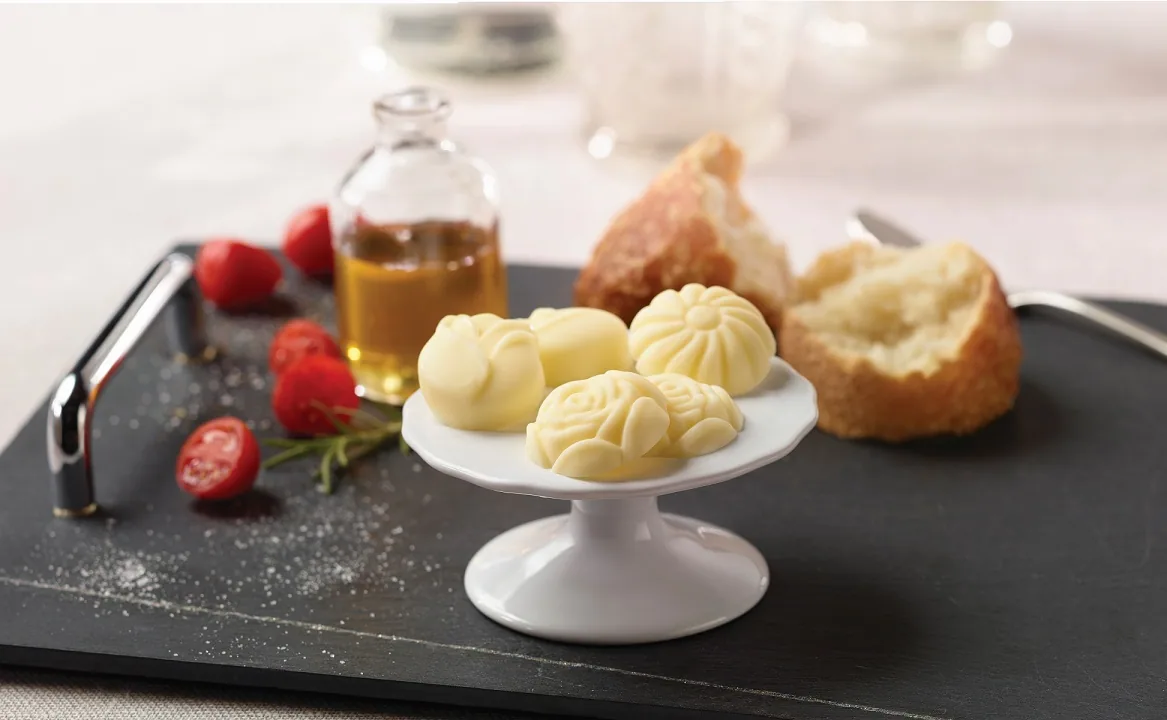 Rose-shaped butter pieces on a pedestal stand with bread and tomatoes