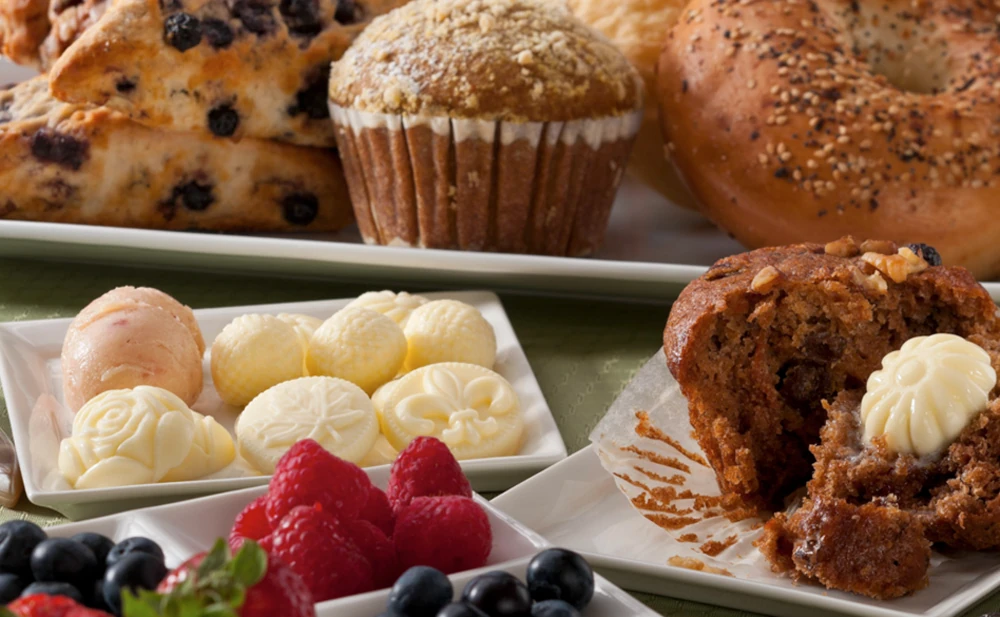 Rosette and shell-shaped butter pats on a plate with pastries and berries