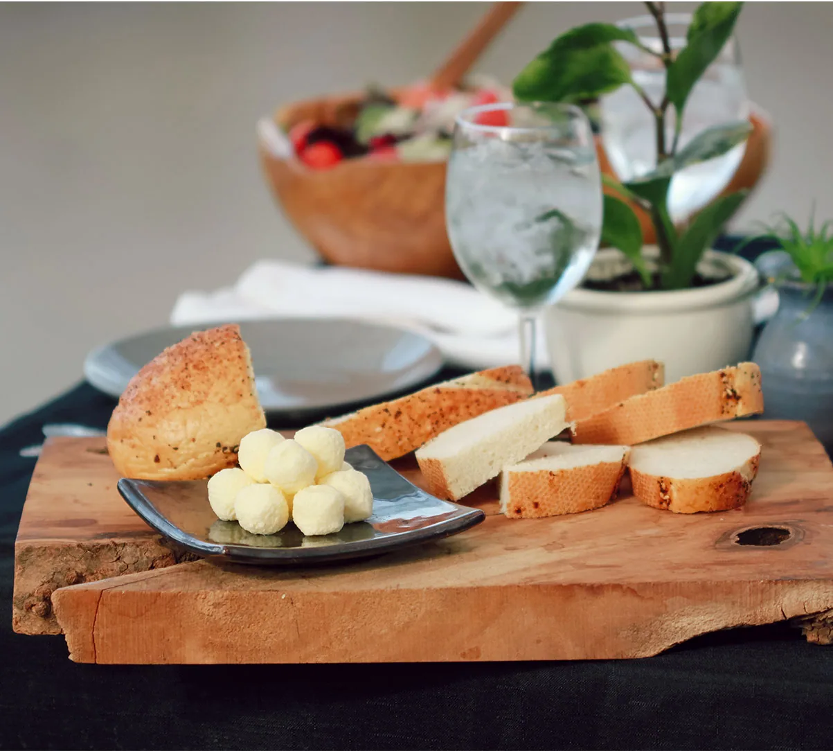 Small round butter balls on a black plate beside sliced bread