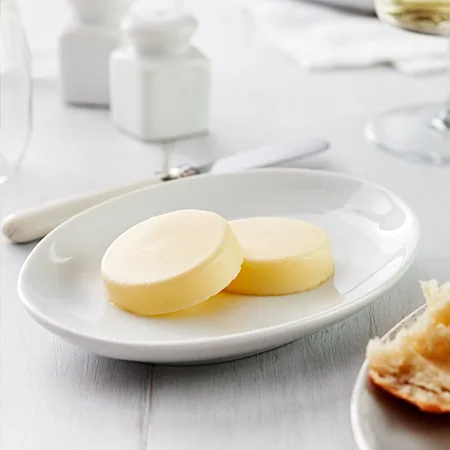 Two round butter pats on an oval plate with salt and pepper shakers