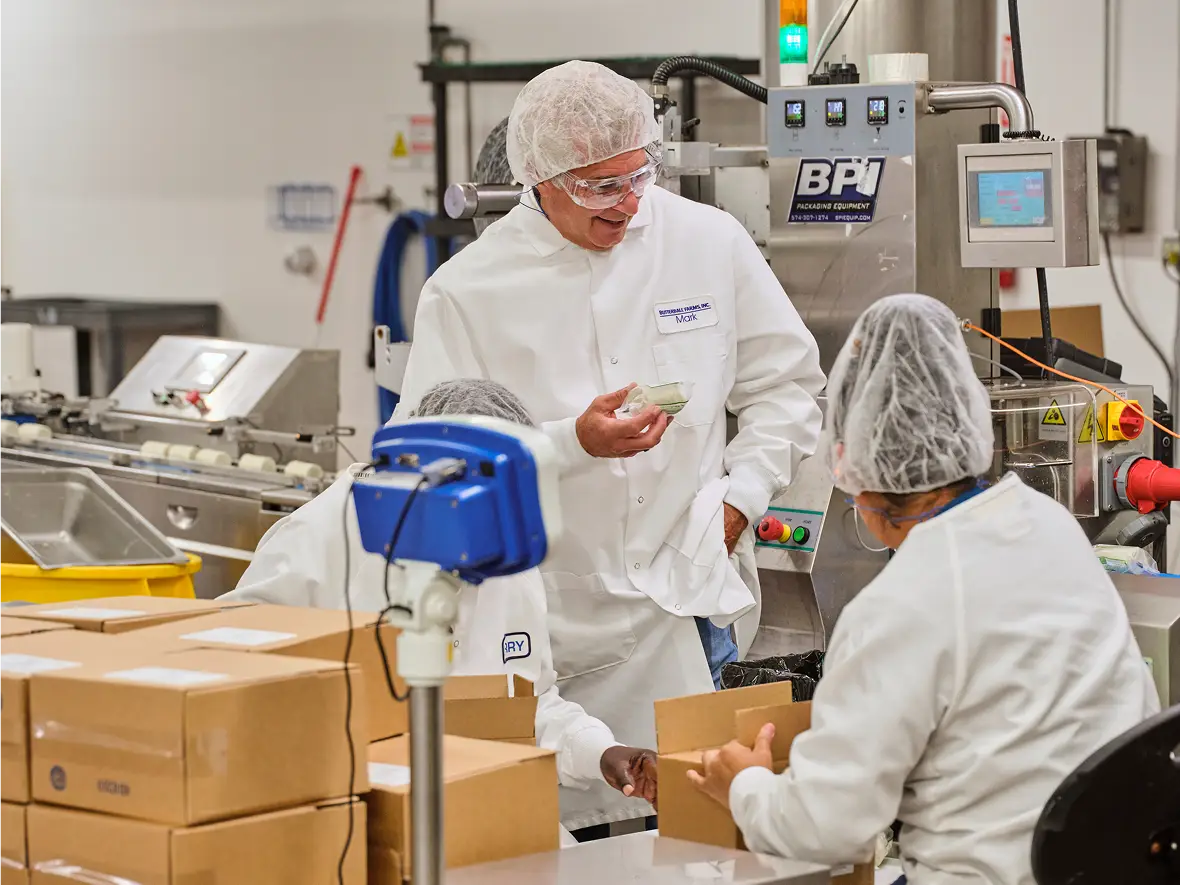 Two Butterball Farms food scientists in lab coats, hairnets and masks reviewing data on a tablet in the production facility