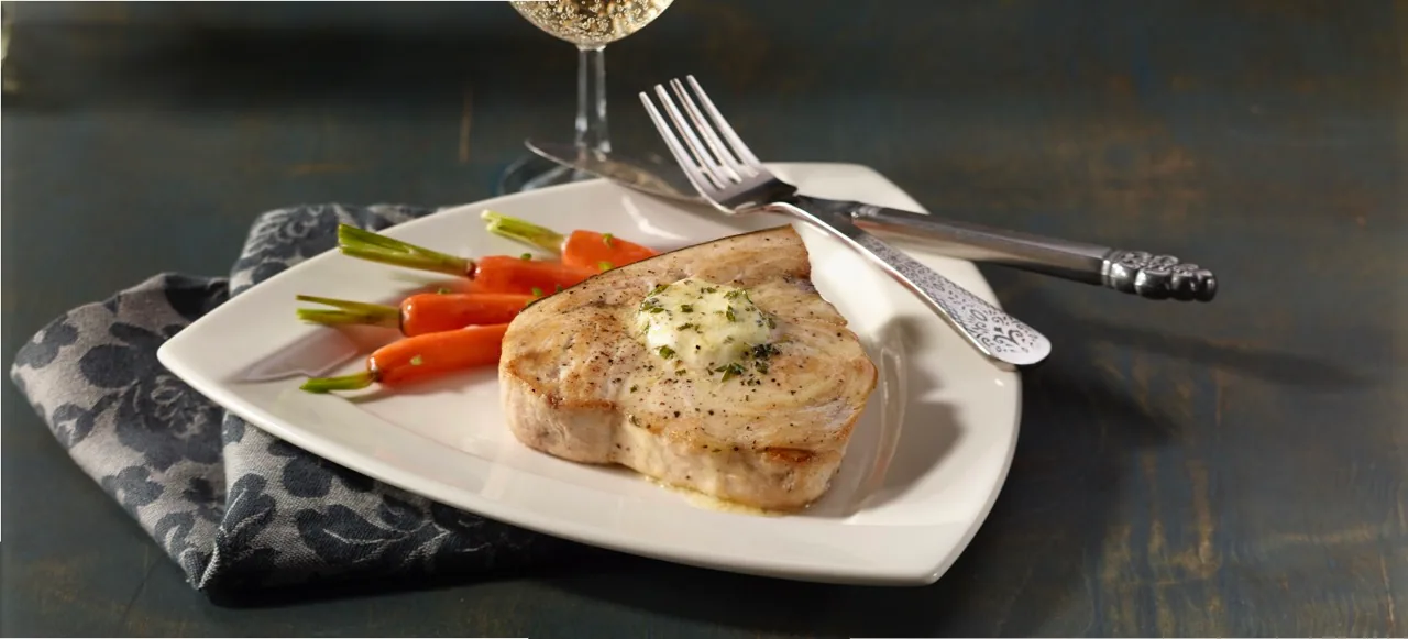 Seared swordfish steak topped with herb butter beside carrots and green beans