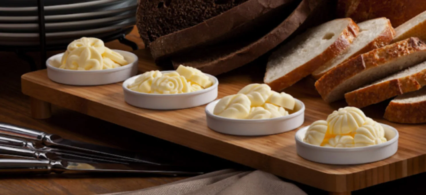 Four dishes of shaped butter pats beside loaves of bread