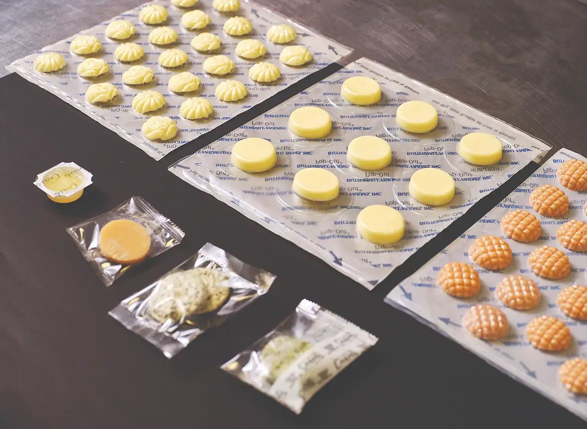 An assortment of flavored butter dollops in herb, spice, and fruit varieties arranged on a white surface